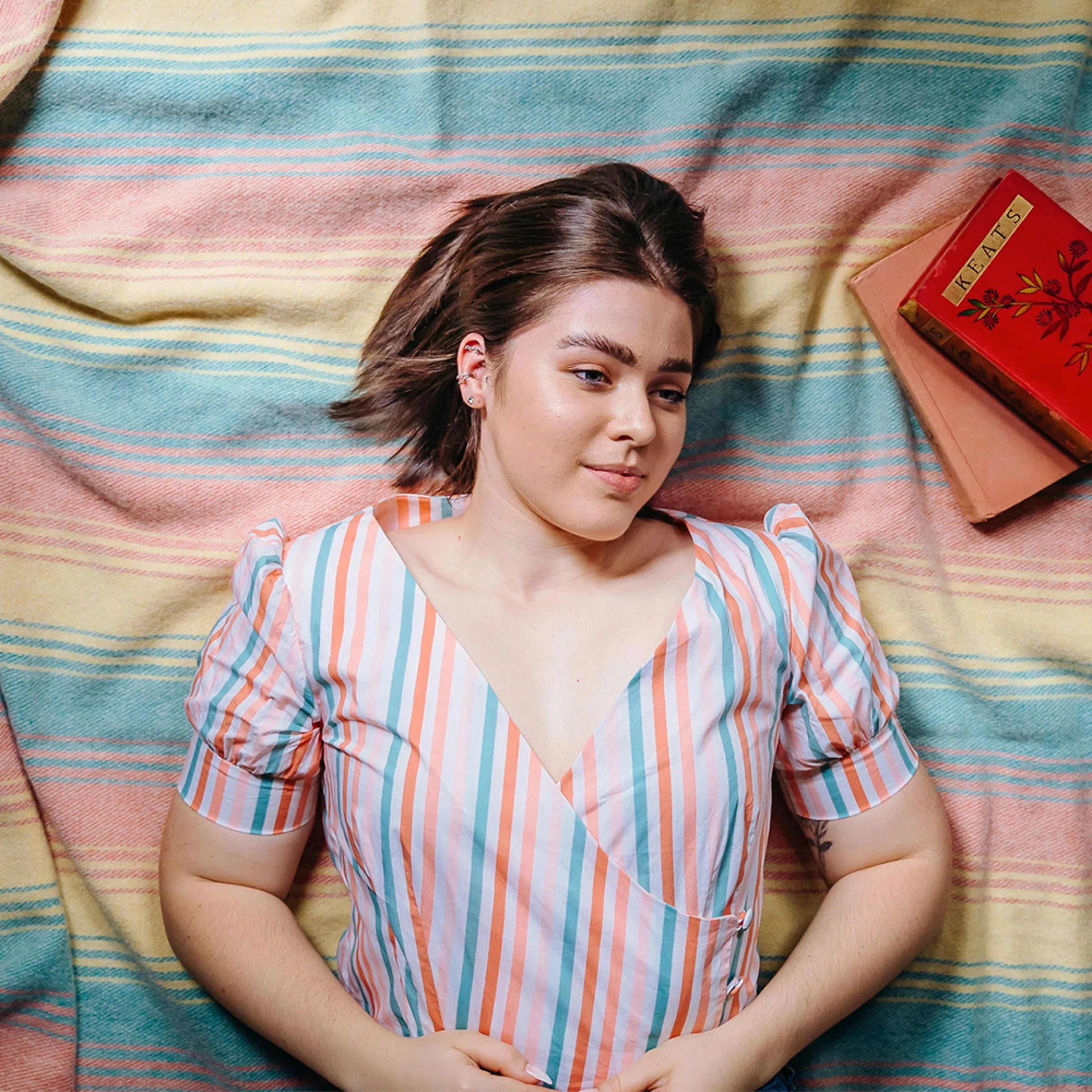 Woman wearing a pink and blue striped blouse while laying on a picnic blanket.